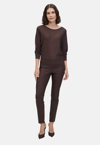 Brązowy metaliczny sweter z szerokim dekoltem, długimi rękawami i prążkowanym wykończeniem, w połączeniu z dopasowanymi brązowymi spodniami i czarnymi szpilkami.