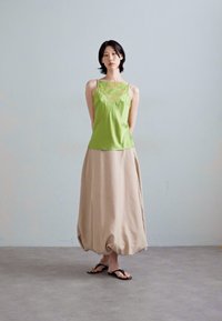 Green satin top with lace accents, paired with a light beige, voluminous, ankle-length skirt. Black flip-flops complete the outfit.