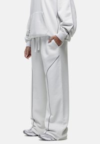 Lichtgrijze katoenen hoodie met grote voorzak, gecombineerd met bijpassende wijde sweatpants met contrasterende donkere naden en zakken.
