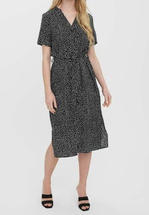 Black midi dress with white polka dots, short sleeves, a v-neck, and a tied waist. Soft fabric with a slight sheen and a flowing skirt.