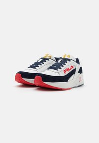 Hvite og marineblå sneakers med røde detaljer, laget av mesh og semsket skinn. Har snøring, polstret tunge og "Fila"-logo på siden.