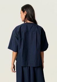 Navy blue short-sleeve shirt with a loose fit, square cut, and a simple collar. Features soft, smooth fabric and a clean, minimal design.