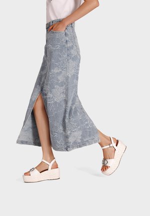 Gonna maxi in denim azzurro chiaro con spacchi laterali, caratterizzata da un delicato motivo floreale, abbinata a sandali con piattaforma bianchi e cinturini alla caviglia.