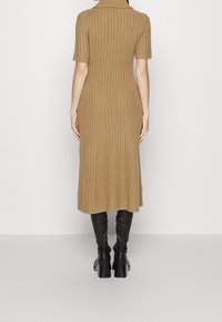 Brun ribstrikket kjole med krave, korte ærmer og længde til midt på læggen, kombineret med knælange sorte læderstøvler.