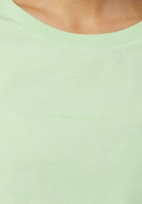 Light green cotton t-shirt with a crew neck and subtle embossed text "CASUAL IDENTITY" near the neckline. Soft, smooth texture.