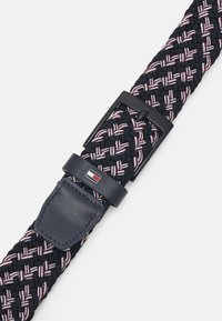 Cintura tessuta blu navy con accenti rossi e bianchi, fibbia in metallo nero e anello in pelle con dettaglio del logo. Materiale morbido e strutturato.