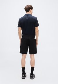 Μπλε ναυτικ ή πόλο μπλούζα με κοντά μανίκια, συνδυασμένη με μαύρο σορτς. Το σορτς διαθέτει δύο πίσω τσέπες και ένα μικρό κεντημένο λογότυπο στην δεξιά τσέπη.