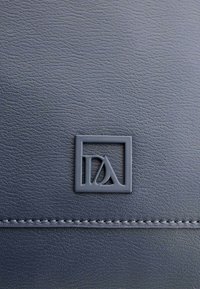 Cuero texturizado azul oscuro con un logo cuadrado en relieve en el centro y una línea de costura contrastante en la parte inferior.