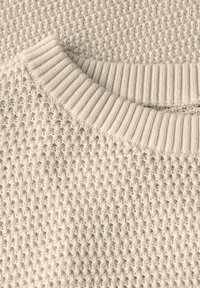 Beige tekstuurellinen neulepaita, jossa on ribbikuvioitu pyöreä pääntie. Kangas on hunajakenno-kuosisesti ja pehmeän näköinen.