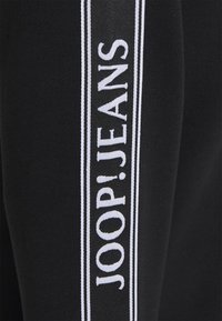 Černé tepláky s bílým vertikálním logem "JOOP!JEANS", s hladkou, jemnou texturou a přiléhavým střihem.