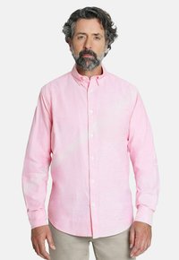 Camisa de botón rosa claro con mangas largas, cuello abotonado y una textura sutil. Usada con pantalones beige.
