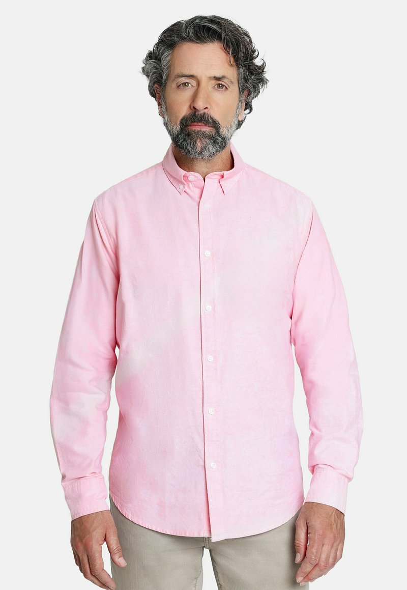 Camisa de botón rosa claro con mangas largas, cuello abotonado y una textura sutil. Usada con pantalones beige.