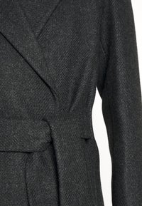Manteau en laine gris foncé avec un motif en chevrons, doté d'un large col à revers et d'une ceinture en tissu épais nouée à la taille.