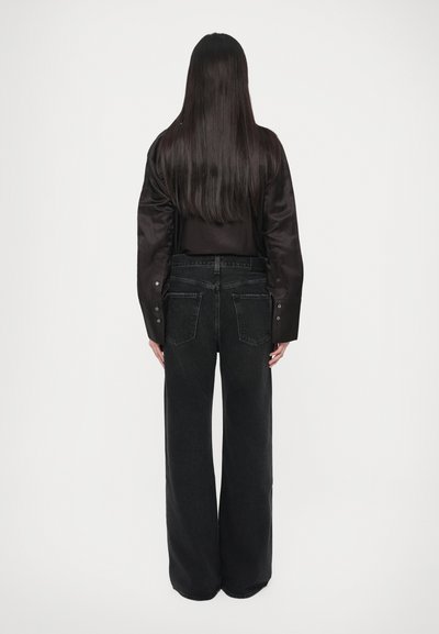 Μαύρο πουκάμισο και μαύρο τζιν με φαρδιά μπατζάκια. Το πουκάμισο έχει μακριά μανίκια και κουμπιά. Το τζιν έχει ψηλή μέση με τσέπες στο πίσω μέρος.