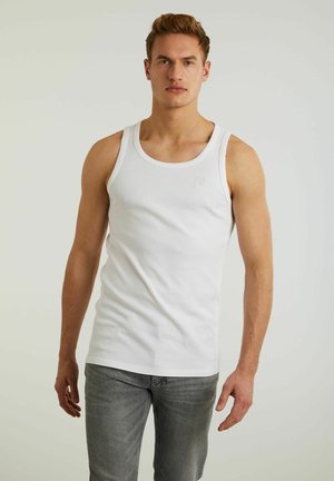 Débardeur en coton blanc avec de larges bretelles, un col rond et un logo brodé subtil sur la poitrine. Porté avec un jean gris.