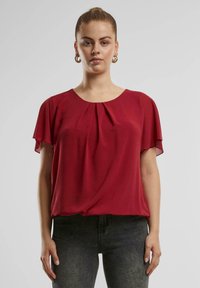 Rode blouse met korte mouwen en een ronde halslijn met plooien, gemaakt van een zachte, vloeiende stof. Gecombineerd met donkere, slim-fit jeans.