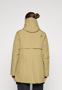 Ljus olivgrön vattentät jacka med hög krage, rundad huva och lagerdesign på baksidan. Har minimal varumärkeslogotyp och långa ärmar.