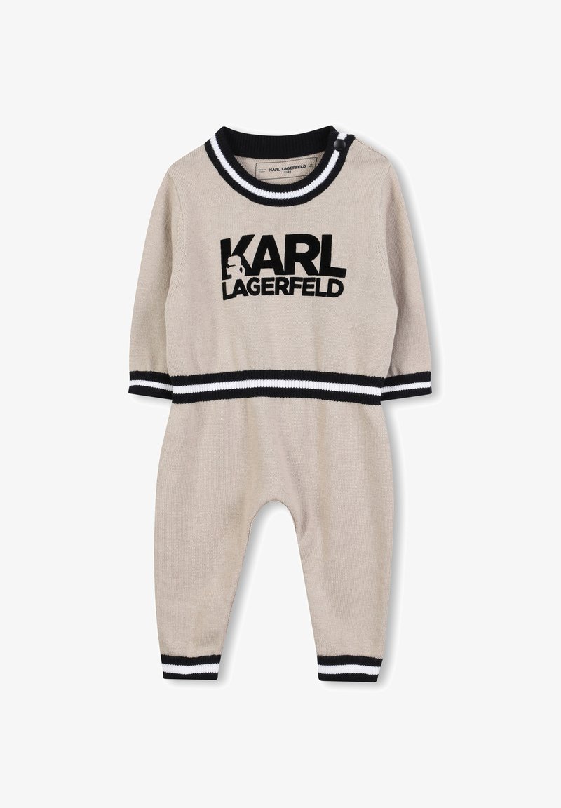 Combinaison en tricot beige avec des accents rayés noir et blanc, arborant le logo "KARL LAGERFELD" sur le devant et une fermeture à pression à l'épaule.