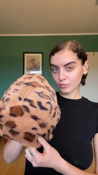 Puha, barna plüss anyagból készült, fekete leopárd foltos kerek sapka. Felszíne kerek, széle visszahajtott, és nincs látható fémrész vagy dísz.