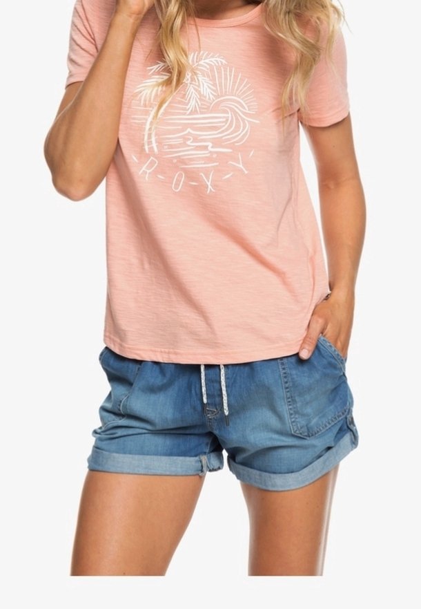 T-shirt rose clair avec un motif de palmier blanc et le texte "Roxy". Associé à un short en denim retroussé avec taille à cordon et poches.