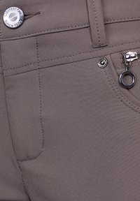 Grijze stoffen broek met een gladde textuur, een zichtbare rits met een ringtrekker en een metalen knoop met branding.