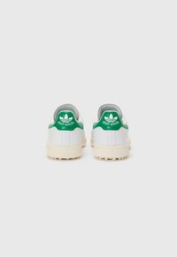 Bílé tenisky s zelenými akcenty, vyrobené z hladké kožené svršky, s kulatou patou a texturovanou gumovou podrážkou. Logo "Stan Smith" na patě.