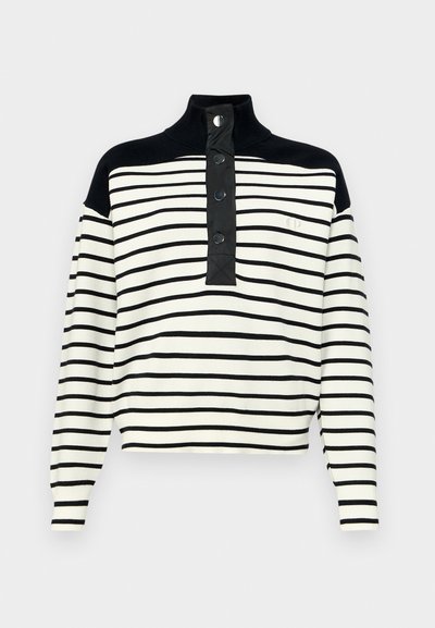 Svart-og-hvittstripet genser med høy krage, knappestolpe og svarte skulderdetaljer. Myk tekstur med en avslappet passform.