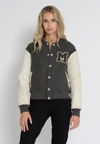 Grå uldjakke med cremede quiltede lædersleeves, trykknapper og et mørkt "M"-patch på brystet. Ribbet manchetter og kant.