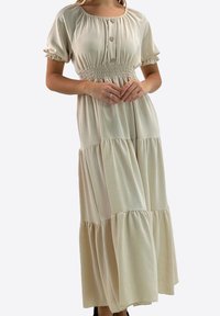 Maxikjole i cremefarve med smocktalje, korte pufærmer, knapper foran og lagdelt flæsedetalje nederst.