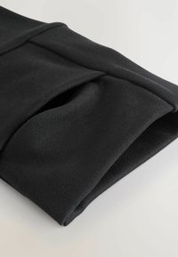 Schwarzer Stoffärmel mit glatter Textur und einem umgeschlagenen Bunddesign, das eine Öffnung für die Hände aufweist. Einfache, minimalistische Konstruktion.