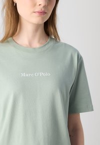 Svetlozelené bavlnené tričko s krátkymi rukávmi a okrúhlym výstrihom. Na prednej strane je bielo natlačený nápis "Marc O'Polo".