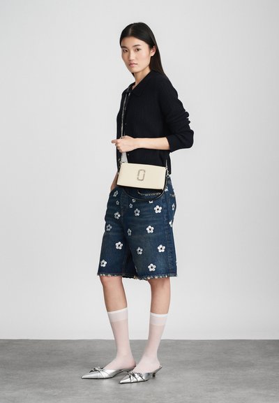 Jeanskjørt med blomstermønster, svart ribbestrikket cardigan, sølvfarne mules og hvite knelengde sokker; liten beige crossover-veske med lås.