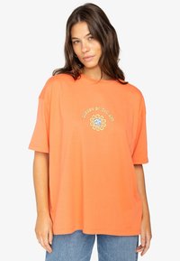 Orange oversized t-shirt made of cotton, featuring a circular sun logo in gold and blue at the center. Short sleeves and crew neckline.