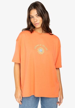 Orange oversized t-shirt lavet af bomuld, med et cirkulært sol-logo i guld og blåt i midten. Korte ærmer og rund halsudskæring.