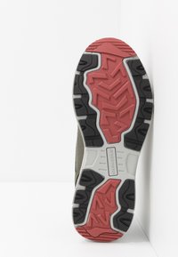 Suela de zapato con un diseño robusto en goma negra, roja y gris. Los patrones texturizados ofrecen tracción; incluye detalles de marca.