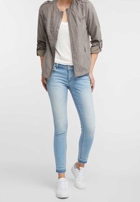 Chaqueta bomber ligera gris con mangas enrolladas, camiseta blanca, jeans ajustados de color azul claro y zapatillas blancas. Conjunto informal de diseño sencillo.