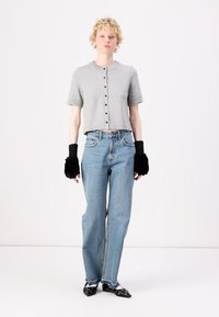 Grauer kurzärmeliger gestrickter Crop-Top mit Knopfverschluss, kombiniert mit hellblauen hoch taillierten geraden Jeans und schwarzen halbärmeligen Fäustlingen aus Kunstfell.