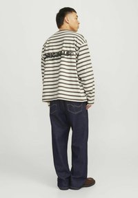 Riba mustriga pikkade varrukatega särk beeži ja pruunis, millel on seljal logo. Kanna tume denim teksadega, rõhutades mugavat istuvust.