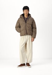Brown puffer jacket with a hood, featuring horizontal quilted sections. Paired with cream-colored loose pants and brown shoes.