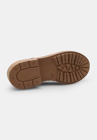 Suola di scarpa in gomma marrone con un motivo di grip testurizzato, punta arrotondata e indentazioni circolari e rettangolari per la trazione.