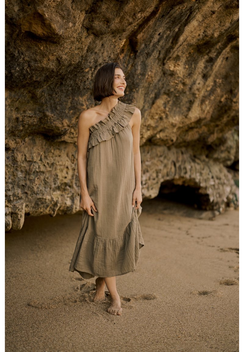 Asümmeetriline ühe õlavarrega kleit tuhmrohelises värvitoonis, millel on frillidega detailid. Voogav kangas, põlvekohale ulatuv, astmelise äärega. Liiv jalgade all.