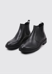 Botas Chelsea de cuero negro con un acabado liso, paneles laterales elásticos y tiradores para ponerlas y quitarlas fácilmente. Suelas de goma planas con un ligero tacón.