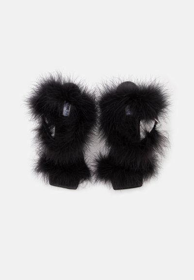 Paire de sandales noires à talons hauts avec des brides en fourrure duveteuse et des bouts carrés sur fond blanc.