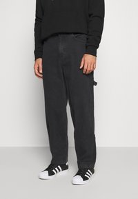 Svarta denimbyxor med lös passform, som har traditionella fickor och en subtil textur, kombinerade med svartvita sneakers.