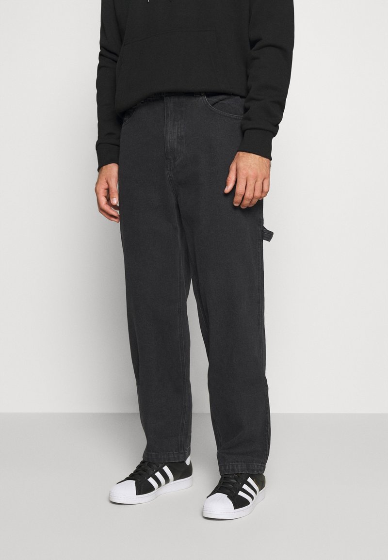 Svarta denimbyxor med lös passform, som har traditionella fickor och en subtil textur, kombinerade med svartvita sneakers.