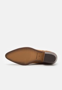 Sole di scarpa in suede color tan, dalla forma appuntita e con una presa testurizzata. Presenta il marchio e i dettagli della taglia sulla soletta. Suola beige liscia.