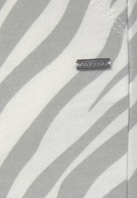 Grau-weiß gestreifter Stoff mit glatter Textur, versehen mit einem metallischen Logoetikett, das den Markennamen trägt.