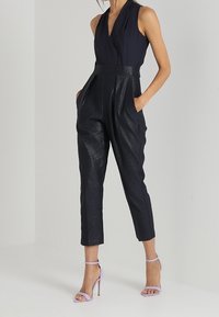 Námořnický overal s hlubokým výstřihem ve tvaru V, přiléhavým pasem a zúženými nohavicemi. Texturovaná tkanina s jemným leskem. V kombinaci s levandulovými sandály na tenkých podpatcích.