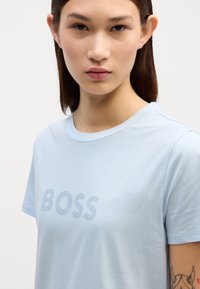 Šviesiai mėlyna, trumpomis rankovėmis marškinėliai, pagaminti iš minkštos medžiagos, su apvaliu kaklu. Priekinėje pusėje turi ryškų, subtilų "BOSS" logotipo dizainą.
