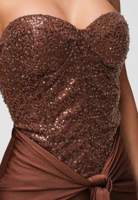Haut corset marron sans bretelles à sequins avec tissu en satin drapé noué à la taille sur une personne au teint moyen.